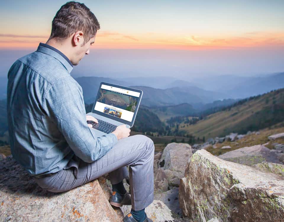 Man using laptop sitting on hill top